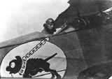 En su aeroplano, mostrando su distintivo con un perro negro jadeante y encadenado.